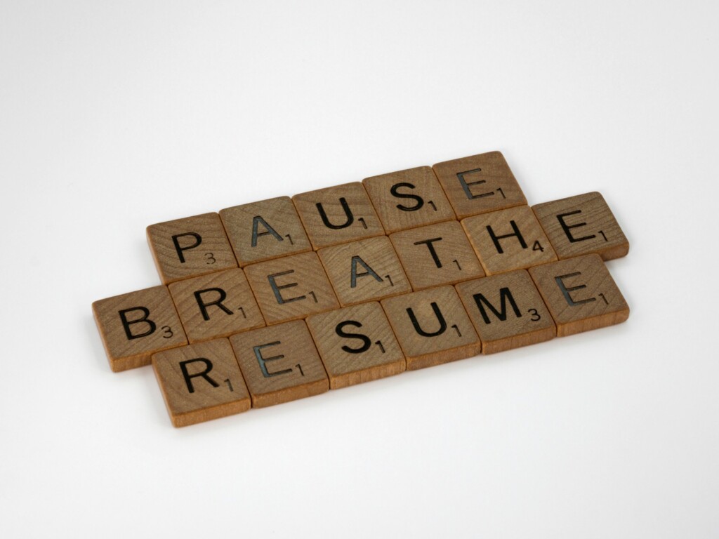 Scrabble tiles spelling out pause, breathe, resume - a reminder to slow down and surrender with awareness.