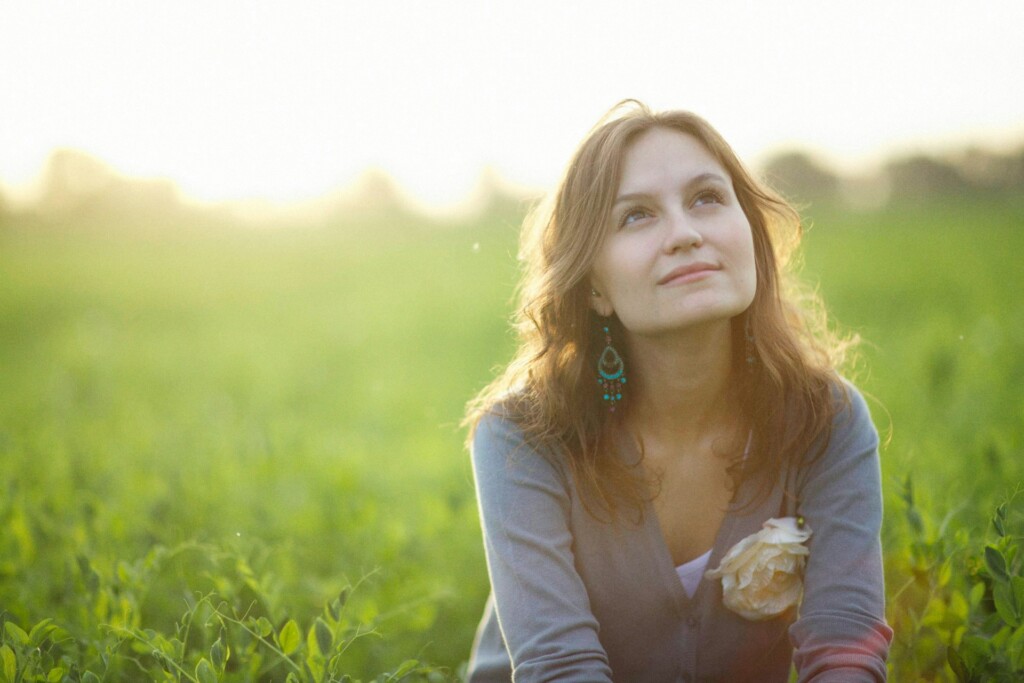 A woman sitting calmly in a green field, looking upward with a soft expression.