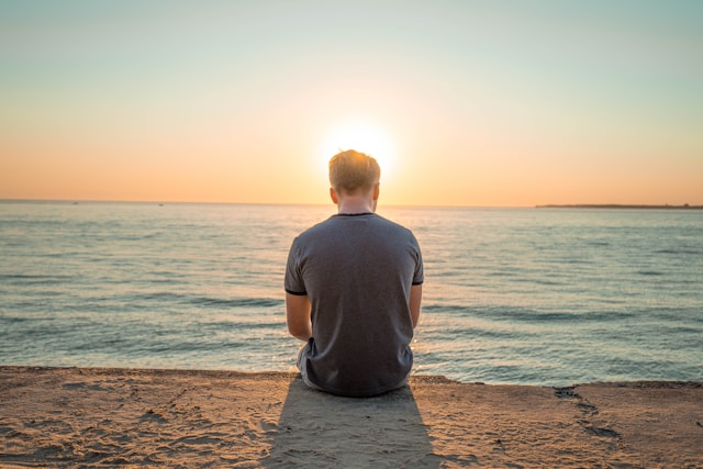 A man sitting by a body of water. 